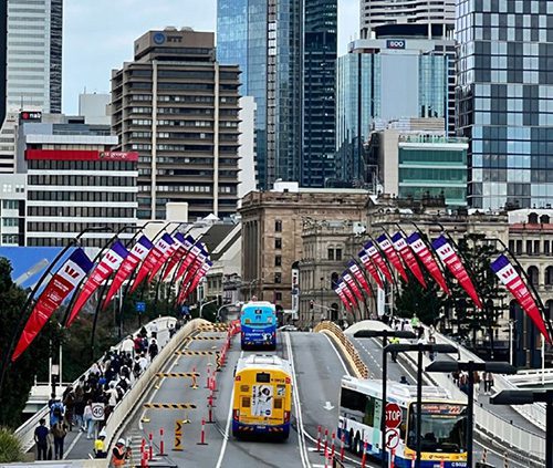 View of a Brisbane bridge with city buildings in the background flying Westpac branded Social Enterprise World Forum flags