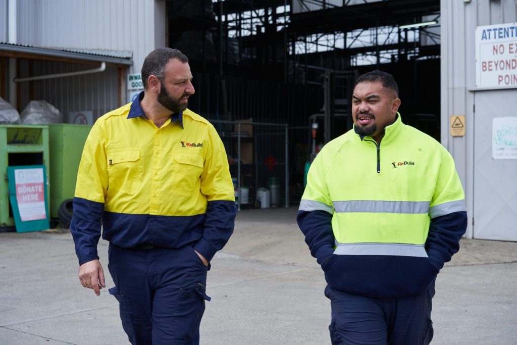 Two employees at YMCA ReBuild walking side by side, talking to each other outside a warehouse.