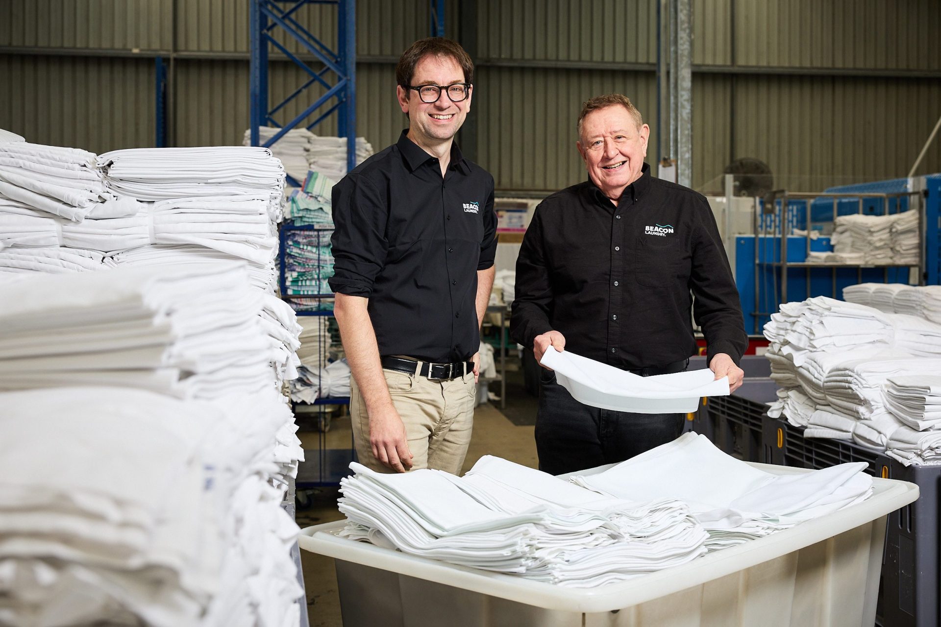 Two men in dark shirts with Beacon logo standing in a laundry