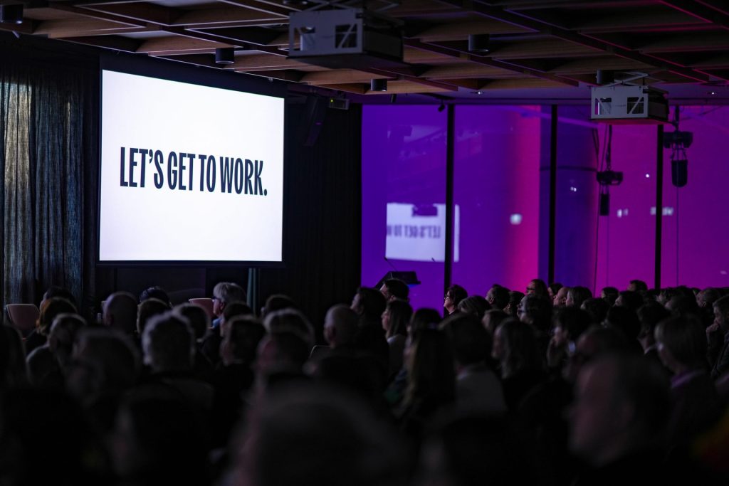 conference room shot from the Social Enterprise jobs Summit with a message on the screen that says: Lets get to work